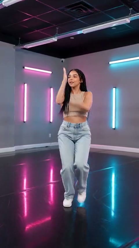 External video still of a solo dancer in jeans and white trainers raising one arm and one foot in a pink-and-cyan neon studio