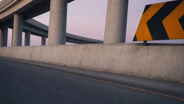 Empty road beneath concrete flyovers with barriers and a yellow-and-black turn sign
